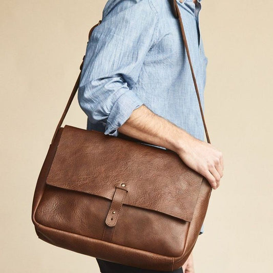 Person holding a brown leather bag against a beige background